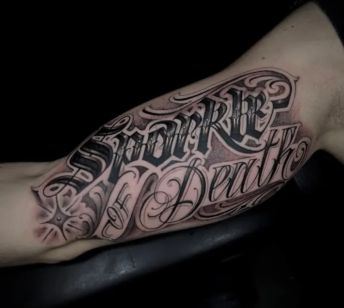 Grande composition de lettres noires et de volutes sur l’avant-bras, par Feel.