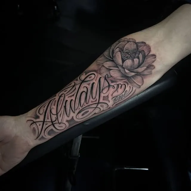 Lettrage noir accompagné d’une fleur sur l’avant-bras, par Feel.