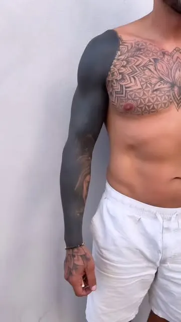Bras couvert d’aplats de noir à côté d’un pectoral tatoué de motifs géométriques, par Mel.
